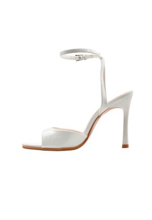Sandalo bianco in pelle verniciata con tacco alto, punta aperta e cinturino alla caviglia, suola beige e tacco a spillo sottile su sfondo bianco.