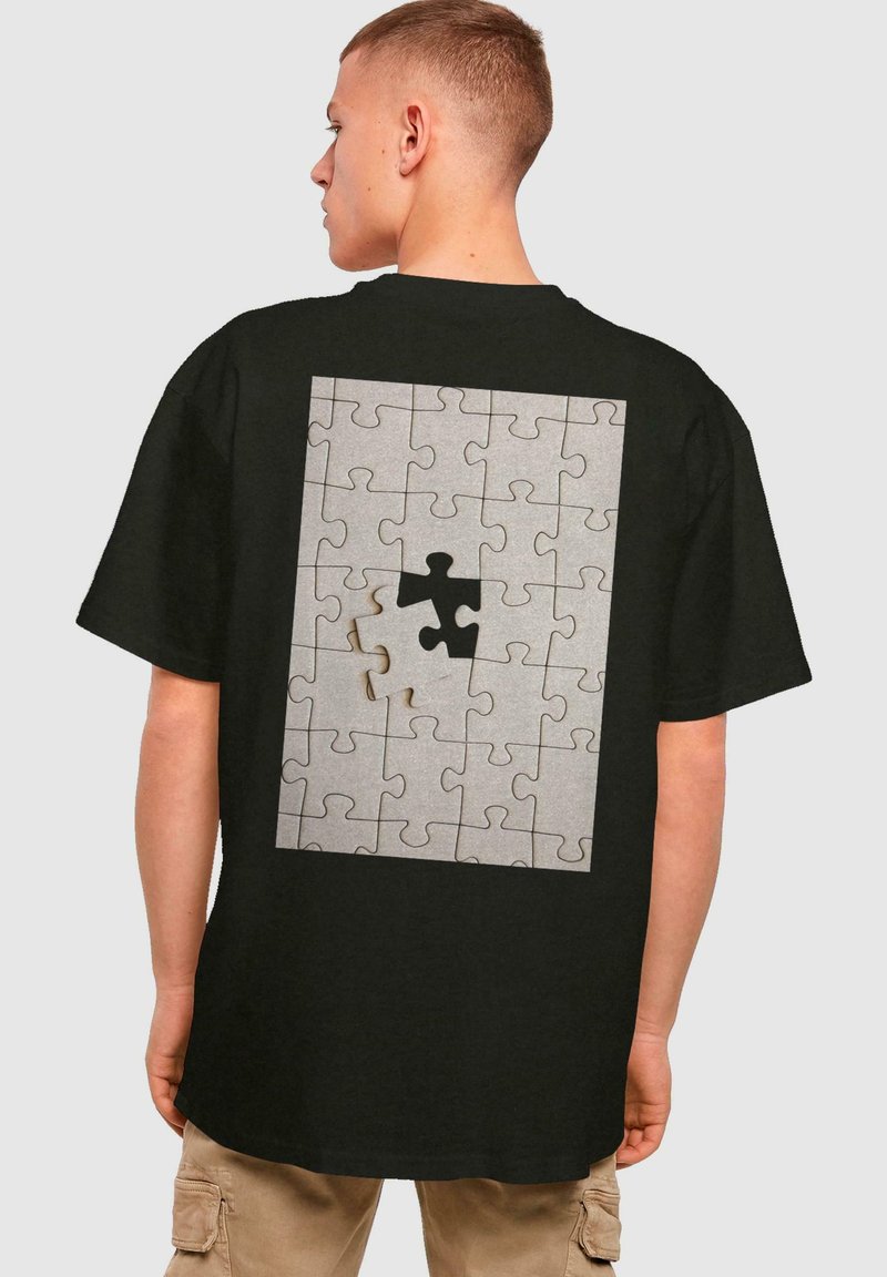 Sort kortærmet t-shirt med et puslespil grafik på bagsiden, hvor en brik mangler, kombineret med grå nuancer og et struktureret design.