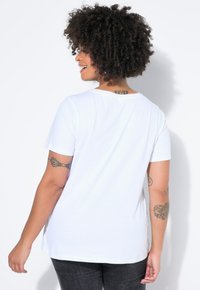 Biały bawełniany t-shirt z krótkimi rękawami i okrągłym dekoltem. Charakteryzuje się luźnym krojem i gładką fakturą. Widok z tyłu ukazuje ozdobne tatuaże.