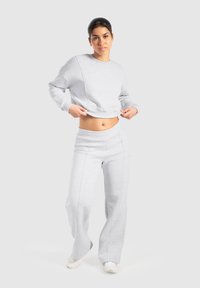 Completo di felpa e pantaloni grigi chiari realizzato in morbido tessuto, con un design cropped, gambe larghe e dettagli di cucitura visibili.