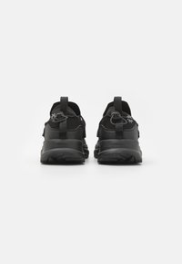 Baskets de sport noires avec une tige en mesh texturé, lacets plats, cols rembourrés et semelles en caoutchouc robustes, avec des languettes de traction à l'arrière.