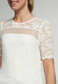 Weißes Spitzentop mit kurzen Ärmeln, floralem Muster, durchsichtigem Netz-Einsatz, gewellten Ärmelsäumen, mit einer glatten Textur und tailliertem Design.