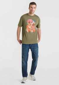 Camiseta verde oliva con un colorido diseño de oso floral, combinada con jeans azules y zapatillas ligeras grises, llevada por un modelo.