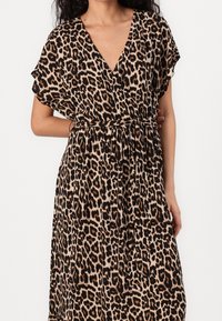 Robe à imprimé léopard avec un col en V, des manches courtes, une taille cintrée et une jupe fluide. Fabriquée en tissu doux avec une finition brillante.