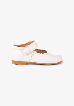 Zapato Mary Jane de cuero blanco con una correa con borde en forma de onda y cierre de botón redondo; suela de goma marrón; textura suave; diseño de punta cerrada.