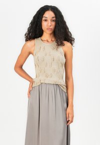 Beige strikket tanktop med tekstureret frynse detaljer, parret med en lys grå plisseret maxinederdel. Glat stof, ærmeløs design.