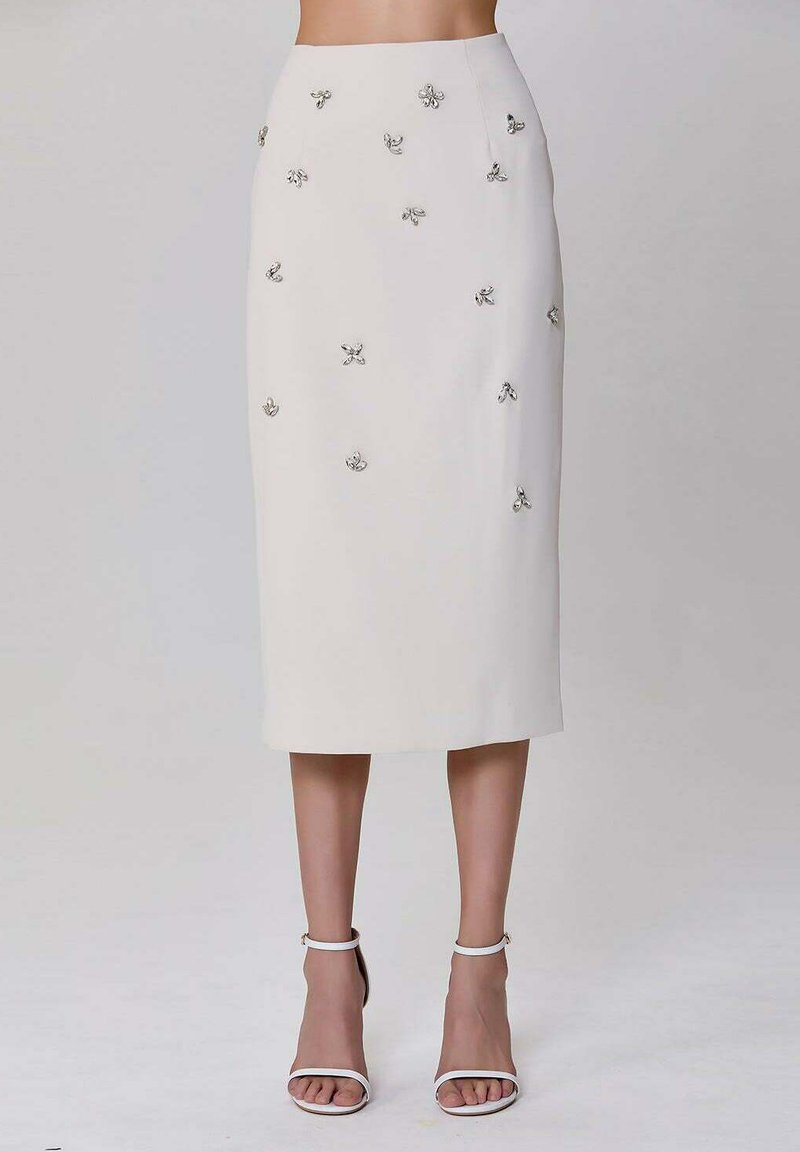 Jupe créme de longueur genou avec des embellissements floraux argentés. Comprend une taille ajustée et un tissu lisse, associée à des talons blancs à lanières.