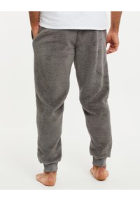 Pantalons de jogging en polaire grise avec une texture douce, des poignets élastiques et des poches latérales, montrés de dos sur un modèle pieds nus.