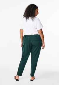 Green elastic-waist trousers with a relaxed fit, featuring two back pockets, paired with a plain white t-shirt. Smooth fabric texture.