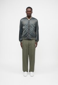 Casaco bomber em verde escuro, acabamento em cetim, com punhos e colarinho canelados. Combinado com calças largas em verde-oliva e ténis brancos.