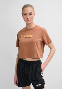 Brun cropped t-shirt med gul "hummel sportswear" tekst, parret med sorte shorts med elastisk talje og logodetalje.