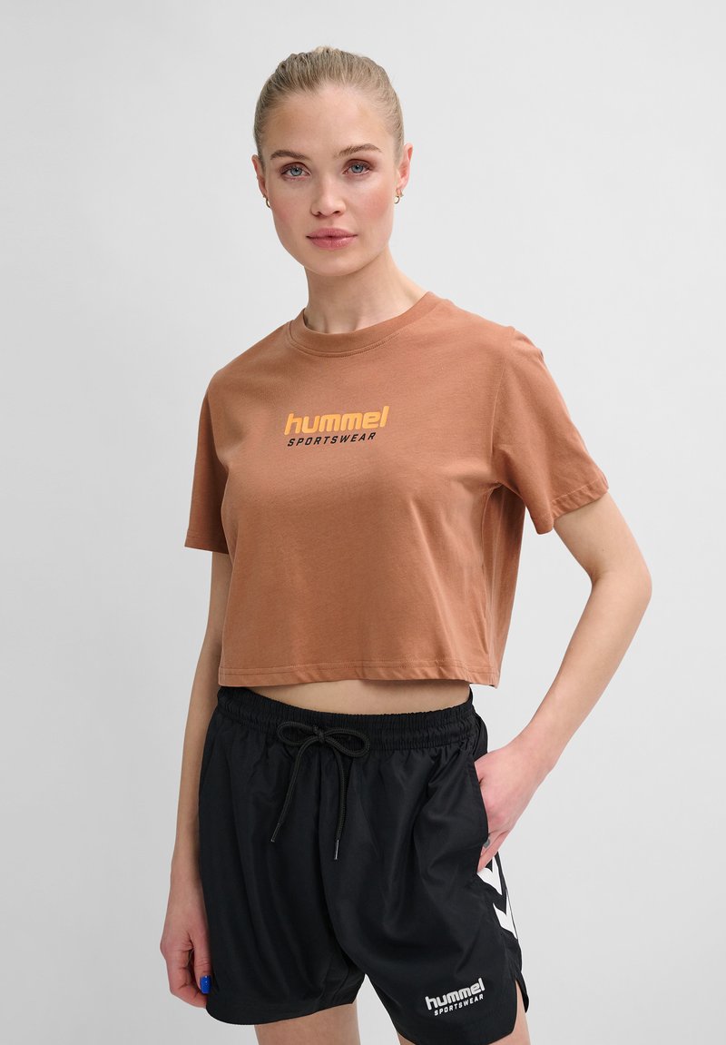Brun cropped t-shirt med gul "hummel sportswear" tekst, parret med sorte shorts med elastisk talje og logodetalje.