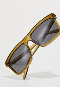 Ochelari de soare dreptunghiulari cu un cadru transparent de culoare chihlimbar, lentile gri și brate elegante, având hardware minim și o textură netedă.