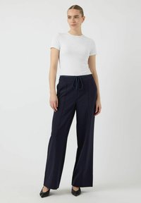 Pantalons larges bleu marine avec taille à cordon, coutures détaillées et texture lisse, associés à un T-shirt ajusté à manches courtes blanc.