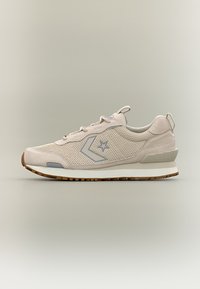 Ανοιχτό μπεζ αθλητικό παπούτσι χαμηλού προφίλ με υφές από δίχτυ και σουέτ, γκρι λογότυπο αστεριού, λευκή σόλα και καφέ λαστιχένια εξωτερική σόλα σε ουδέτερο φόντο.