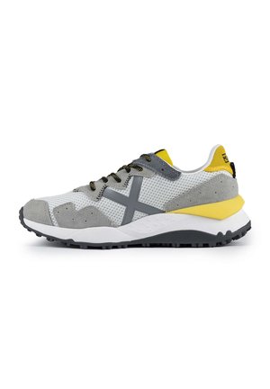 Mannen atletische schoenen met een bovenwerk van gaas in wit en grijs, suède accenten, gele hak, zwarte veters en rubberen zool voor grip.