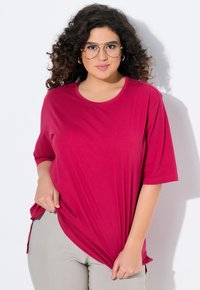 T-shirt fucsia a maniche corte in un tessuto morbido, con scollatura rotonda e spacchi laterali. Abbinato a pantaloni grigio chiaro.