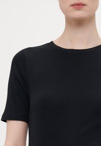 Svart crew-neck t-skjorte laget av myk bomull. Korte ermer med en glatt tekstur og enkelt design, uten synlige mønstre eller dekorasjoner.