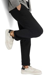 Schwarze Stretchhosen mit Seitentaschen, umgeschlagenen Säumen, kombiniert mit weißen und beigen Sneakers. Glatte Textur mit slim fit Design.
