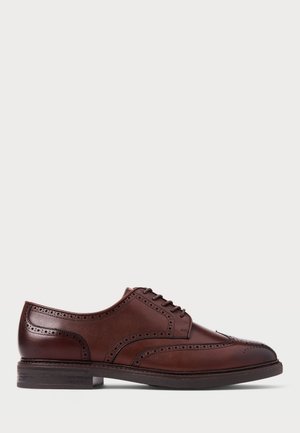 Chaussure brogue en cuir marron avec un design à bouts retournés, des détails perforés et une semelle foncée, présentée en profil latéral sur fond blanc.