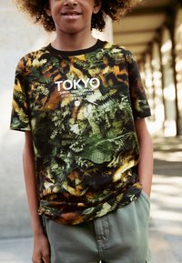 Grünes und braunes kurzärmeliges T-Shirt mit floralem Muster und weißem "TOKYO"-Schriftzug samt Standortkoordinaten. Lässige Passform, weiches Material.