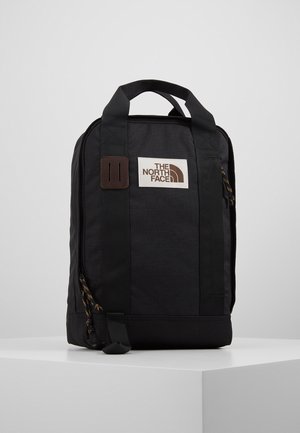 Sac à dos North Face rectangulaire noir avec double poignée supérieure et écusson logo à l'avant sur une surface blanche.