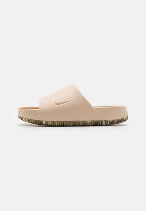 Sandalia tipo slide beige de Nike con una correa ancha y suela texturizada con patrón de camuflaje, mostrada de perfil sobre un fondo blanco.