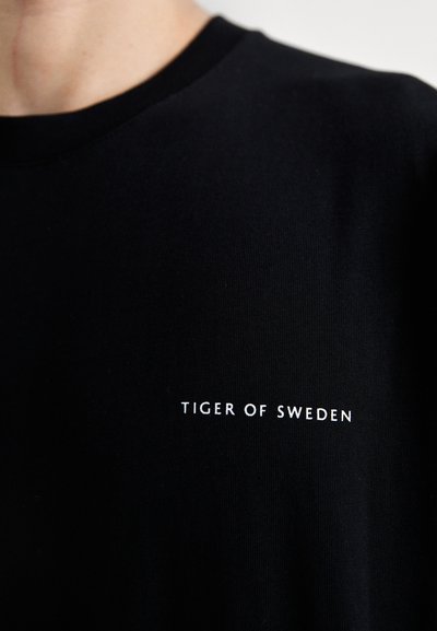 Must must t-särk ringkraega; esiküljel valge kiri "TIGER OF SWEDEN". Pehme tekstuur, keha järgiv disain.