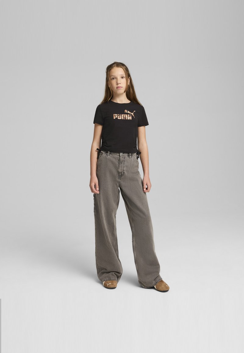 Camiseta negra con gráfico "PUMA", pantalones amplios grises y zapatos marrones. Diseño simple con lazos en los lados de la camiseta. Texturas suaves.