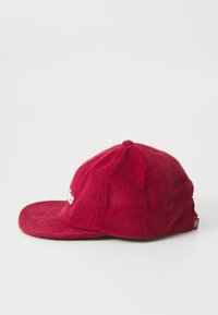 Casquette en velours côtelé rouge avec une visière plate et un tissu texturé. Présente des coutures subtiles et un logo brodé à l'avant.