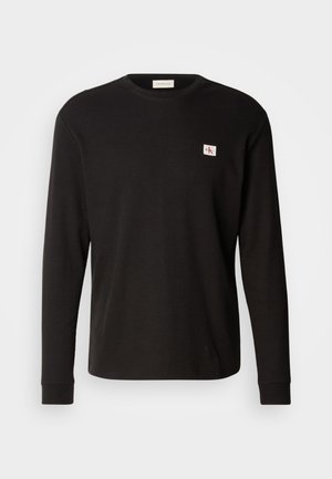 Fekete hosszú ujjú bordázott, kerek nyakú póló kis fehér és piros Calvin Klein logóval a bal mellrészen.