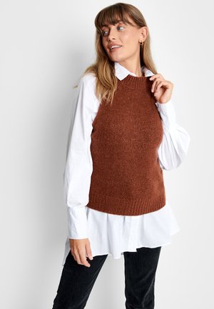 Brauner, gestrickter ärmelloser Pullover mit strukturiertem Finish, getragen über einem weißen Hemd mit Knopfleiste, kombiniert mit schwarzen Hosen.