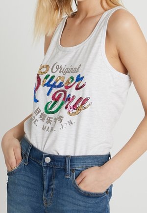 Canottiera grigia con logo "Super Dry" in paillettes colorate; tessuto morbido, scollatura rotonda e spalline larghe; abbinata a pantaloni corti in denim blu.