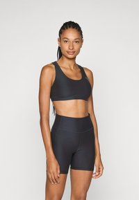 Svart treningstop og høyhullede shorts laget av elastisk stoff. Har en jevn tekstur, brede stropper og subtile sømmer.