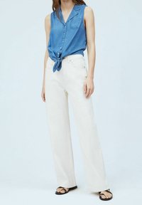 Vaaleanpesuinen denimi ilman hihoja oleva paita, jossa on etupainikkeet ja solmittu helma, yhdistettynä korkeavyötäröisiin, leveälahkeisiin valkoisiin housuihin ja litteisiin sandaaleihin.