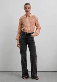 Blusa melocotón con cuello y textura fruncida, de manga larga, combinada con jeans de denim negro de pierna ancha de talle alto.