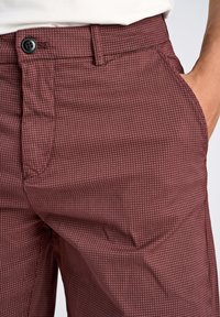 Pantaloni bordeaux con motivo, realizzati in un tessuto testurizzato, dotati di chiusura a bottone e tasche laterali, mostrati all'altezza della vita.