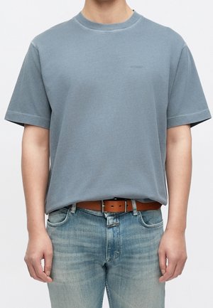 Personne portant un t-shirt à manches courtes bleu clair rentré dans un jean bleu délavé avec une ceinture marron.
