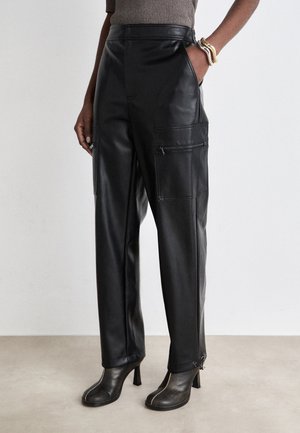 Pantalons en cuir noir à taille haute, avec des poches zippées sur les côtés et une coupe décontractée. Associés à des bottines noires à talons. Texture lisse.