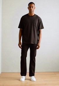 Sort bomuld T-shirt med en brystlomme, parret med mørke bukser og hvide sneakers. Simpel, afslappet pasform med korte ærmer.