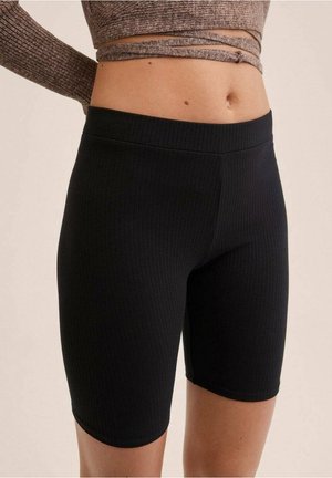 Mujer vistiendo pantalones cortos negros de ciclista de cintura alta con textura acanalada y un top marrón de manga larga recortado con detalle envolvente.