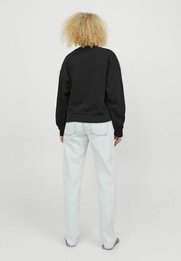 Felpa nera con scollo rotondo e spalle scese, abbinata a jeans dritti di un blu chiaro. Il materiale sembra morbido e informale.