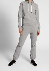 Gråt hoodie- og joggersæt i blødt stof med frontlomme, ribstrikkede manchetter og snoretræk. Kombineret med sorte sneakers.