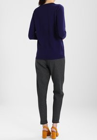 Suéter azul marino de manga larga, combinado con pantalones grises de rayas y sandalias amarillas de tacón bloque. Enfóquese en colores sólidos y líneas limpias.