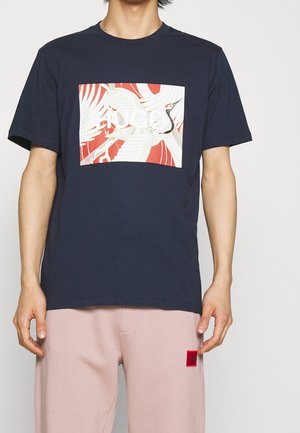 T-shirt en coton bleu marine avec un imprimé graphique blanc d'une grue sur un fond rouge, manches courtes et col rond.