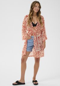 Kimono leggero e semi-trasparente in corallo con motivi astratti di foglie bianche. Presenta maniche lunghe, una cintura da annodare in vita e tasche laterali.