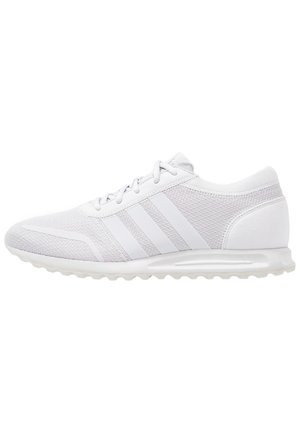 Zapatilla deportiva blanca de corte bajo con parte superior de malla, tres franjas laterales, cierre de cordones y suela acolchada, diseñada para correr o para un uso casual.