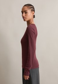 Langermet, tettsittende topp i burgunder, laget av ribbet stoff. Har rund halslinning og glatt tekstur, kombinert med grå, flytende skjørt.