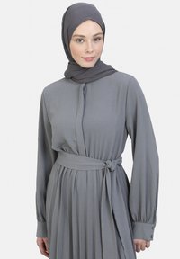 Graues langärmliges Kleid mit tailliertem Oberteil und plissiertem Rock, ergänzt durch einen passenden Schal, einen gebundenen Taillengürtel und Knopfdetails an den Ärmelbündchen.