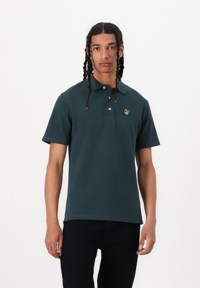 Mørkegrønn polo skjorte laget av bomull, har en klassisk krage, tre-knapps placket og en logo på venstre bryst.